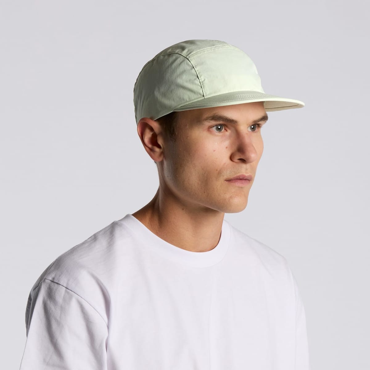 Man in a white t-shirt and light cap looking to the side against a plain background.