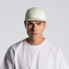 Man in a white shirt and light cap looks straight at the camera against a plain background.