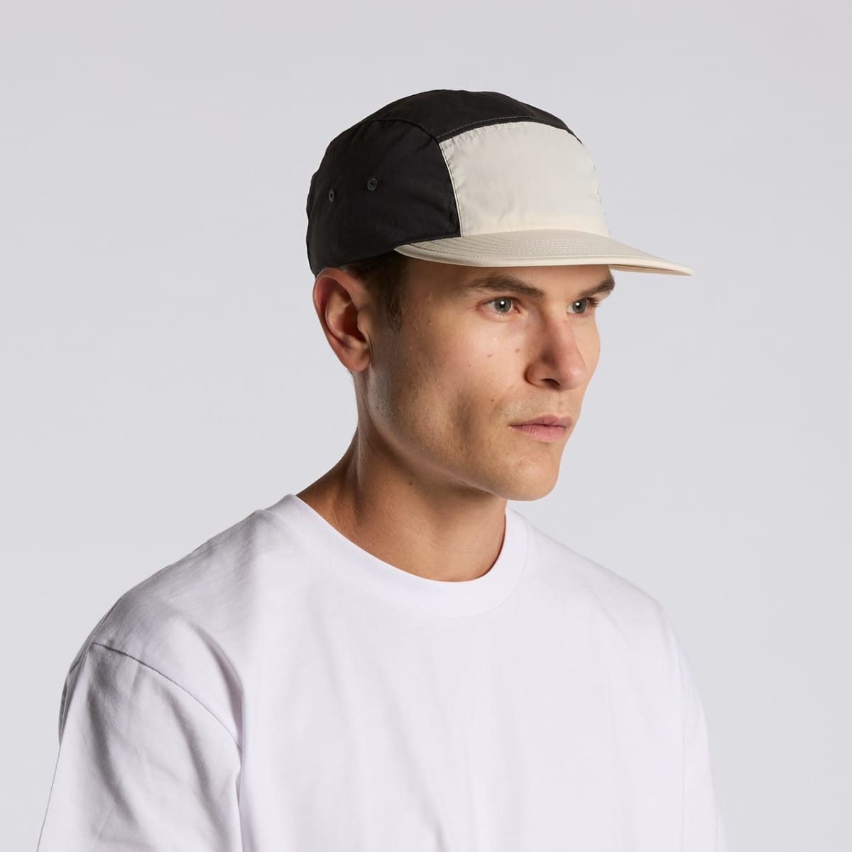 Man in a white t-shirt and two-tone cap looking to the side against a plain background.