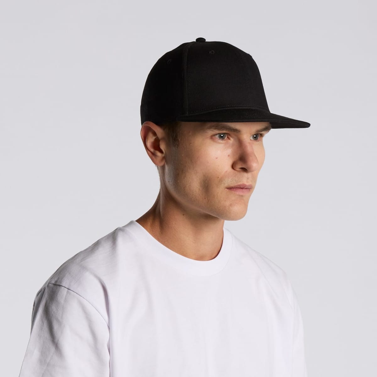 Man in a white shirt and black cap looking to the side against a plain background.
