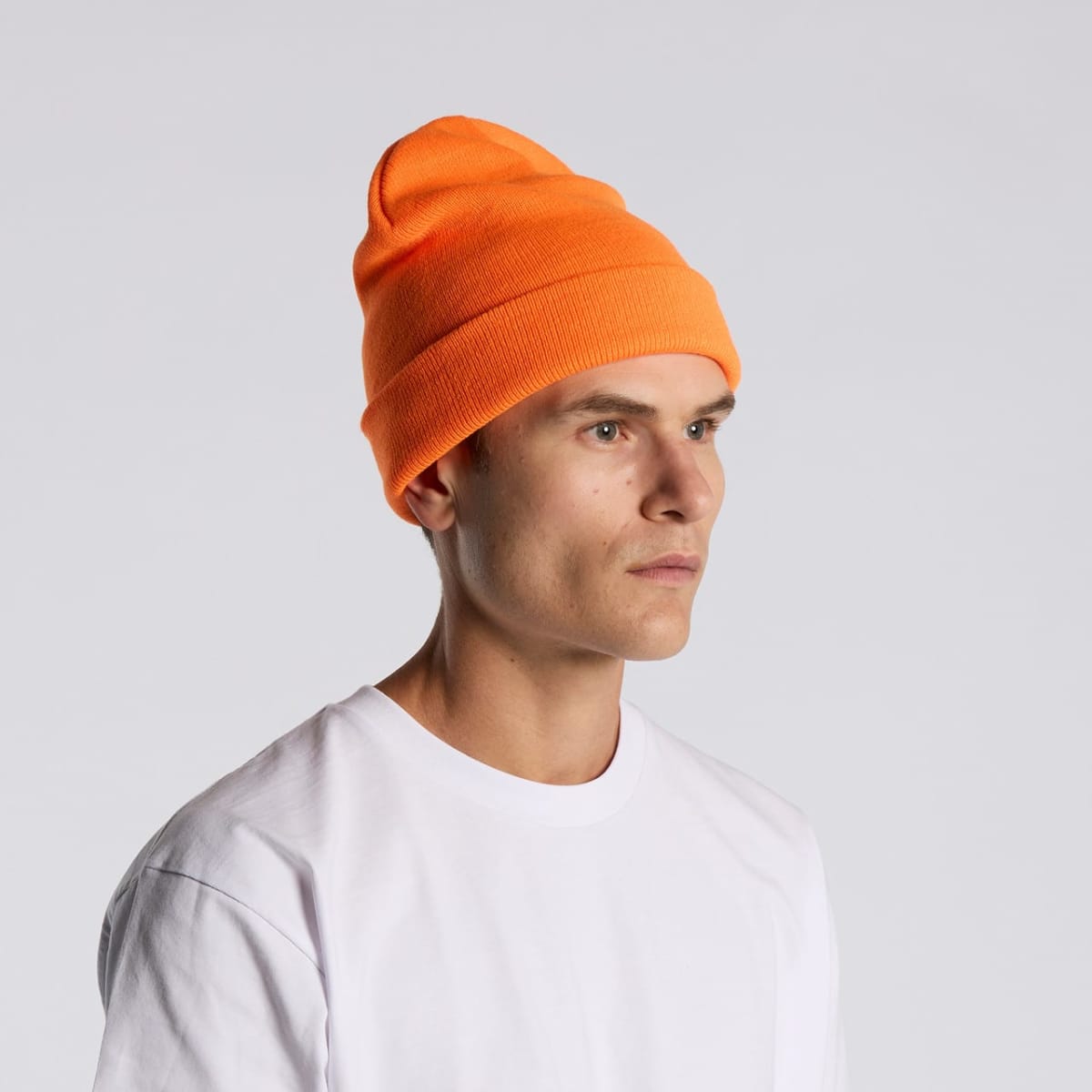 Person wearing an orange beanie and white shirt looking to the side against a gray background.