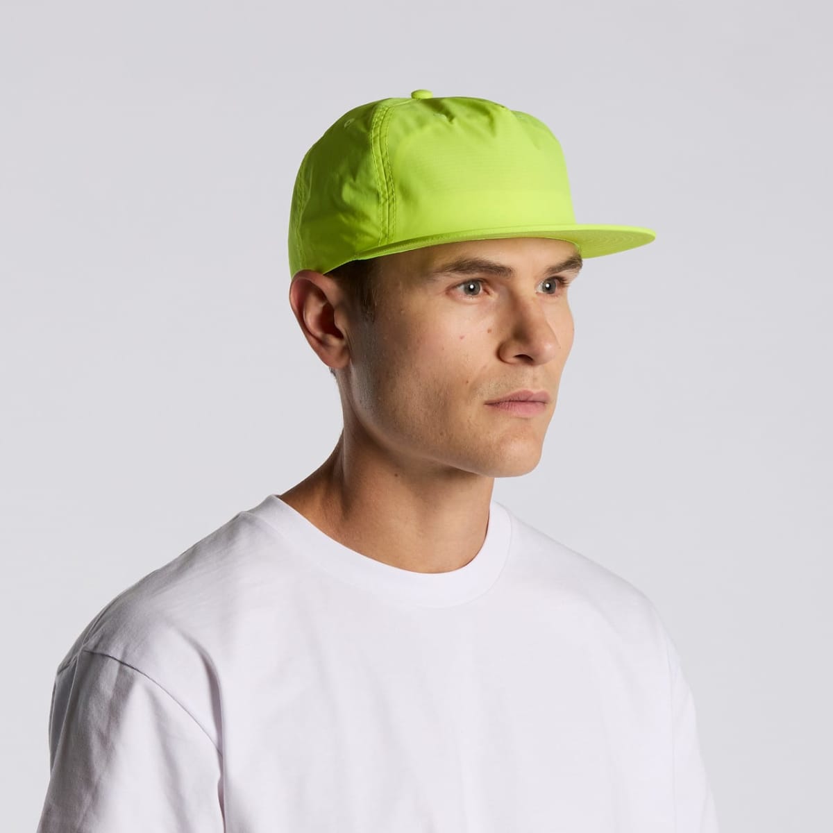 Man in a white shirt and neon yellow cap looks to the side against a plain background.