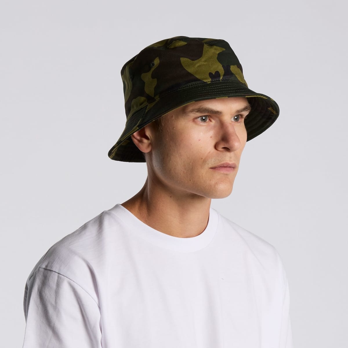 Man in a white shirt wearing a camouflage bucket hat against a plain background.