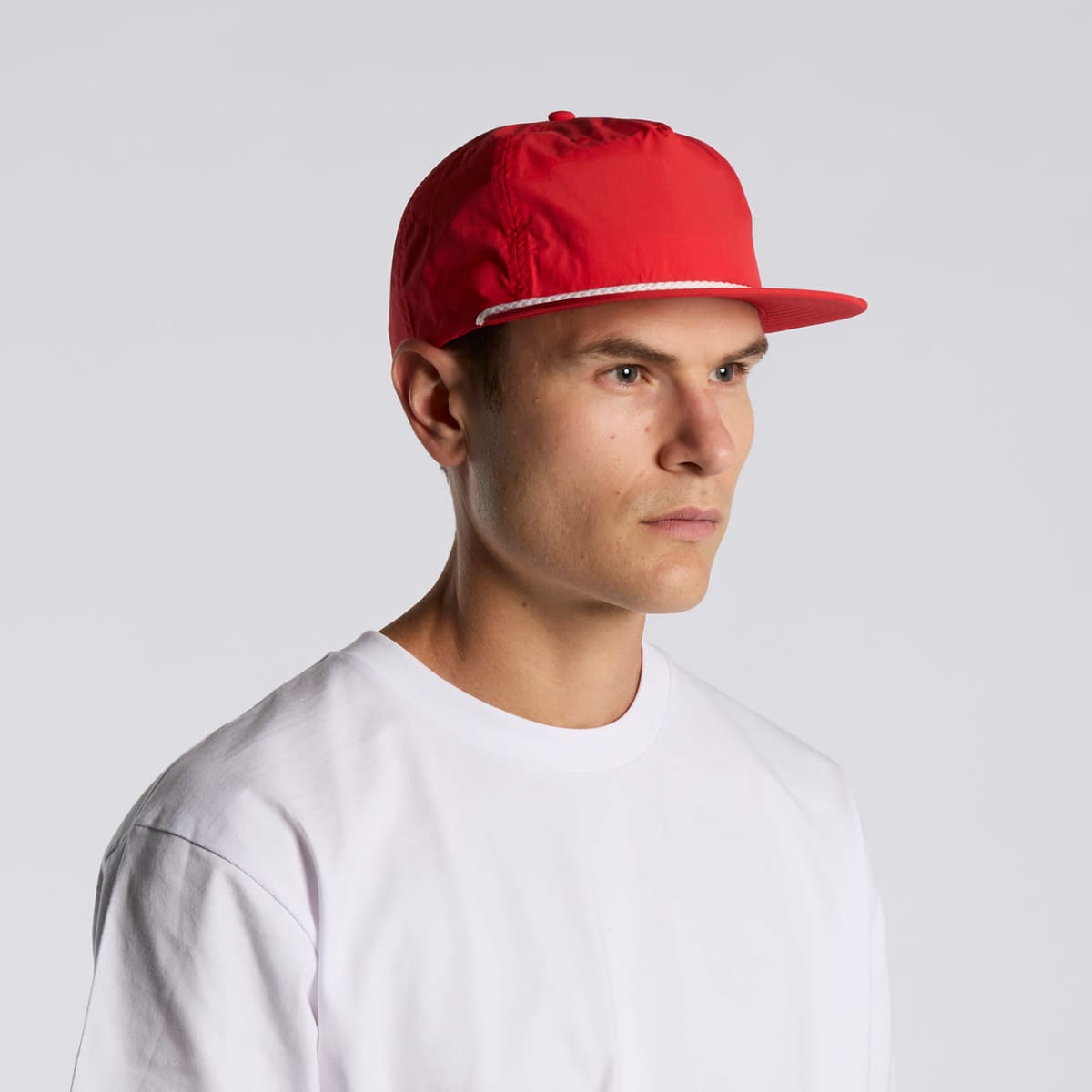 Man in a red cap and white t-shirt looking to the side against a plain background.