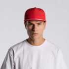 A man in a white shirt and red cap stares seriously at the camera against a gray background.