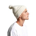Man in a white shirt wearing a white knit beanie with a pom-pom, in profile view.