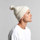 Man in a white shirt and white knit beanie with a pom-pom, facing right.