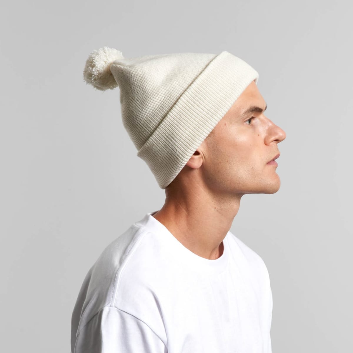 Man in a white shirt and white knit beanie with a pom-pom, facing right.