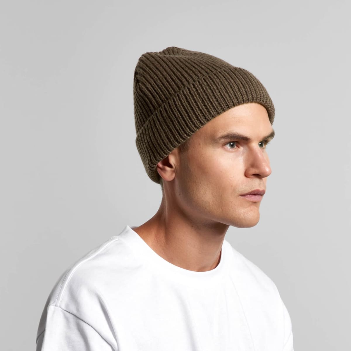 Man in a white shirt and brown knit beanie looks to the side against a gray background.