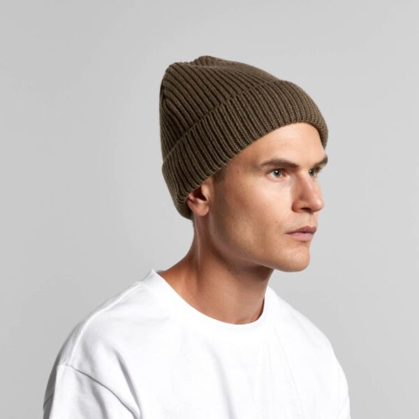 Man in a white shirt and brown knit beanie looking to the side against a plain background.