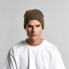 Man in a white shirt and brown knit beanie against a plain light gray background.