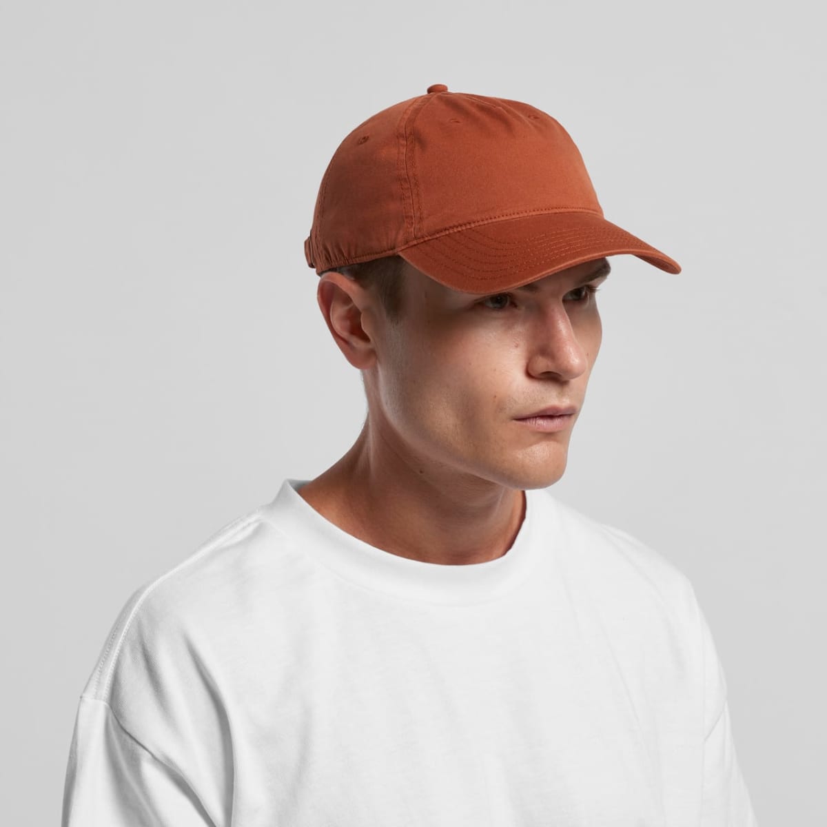 Man in a white t-shirt wearing a rust-colored baseball cap against a plain background.