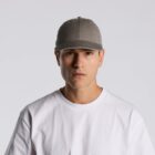 A person in a gray cap and white shirt looks directly at the camera against a plain background.