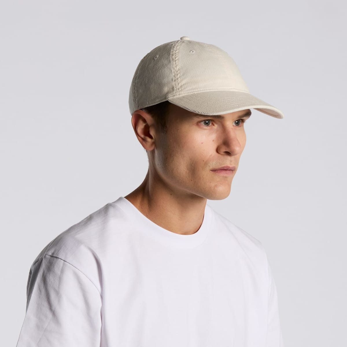 Person in a white t-shirt and cream-colored cap, looking to the side against a gray background.