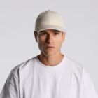 Man wearing a white t-shirt and beige cap against a plain light gray background.