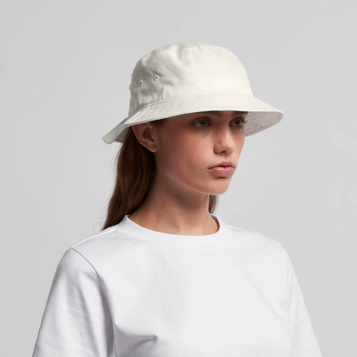 Woman in a white bucket hat and white t-shirt against a plain light background.
