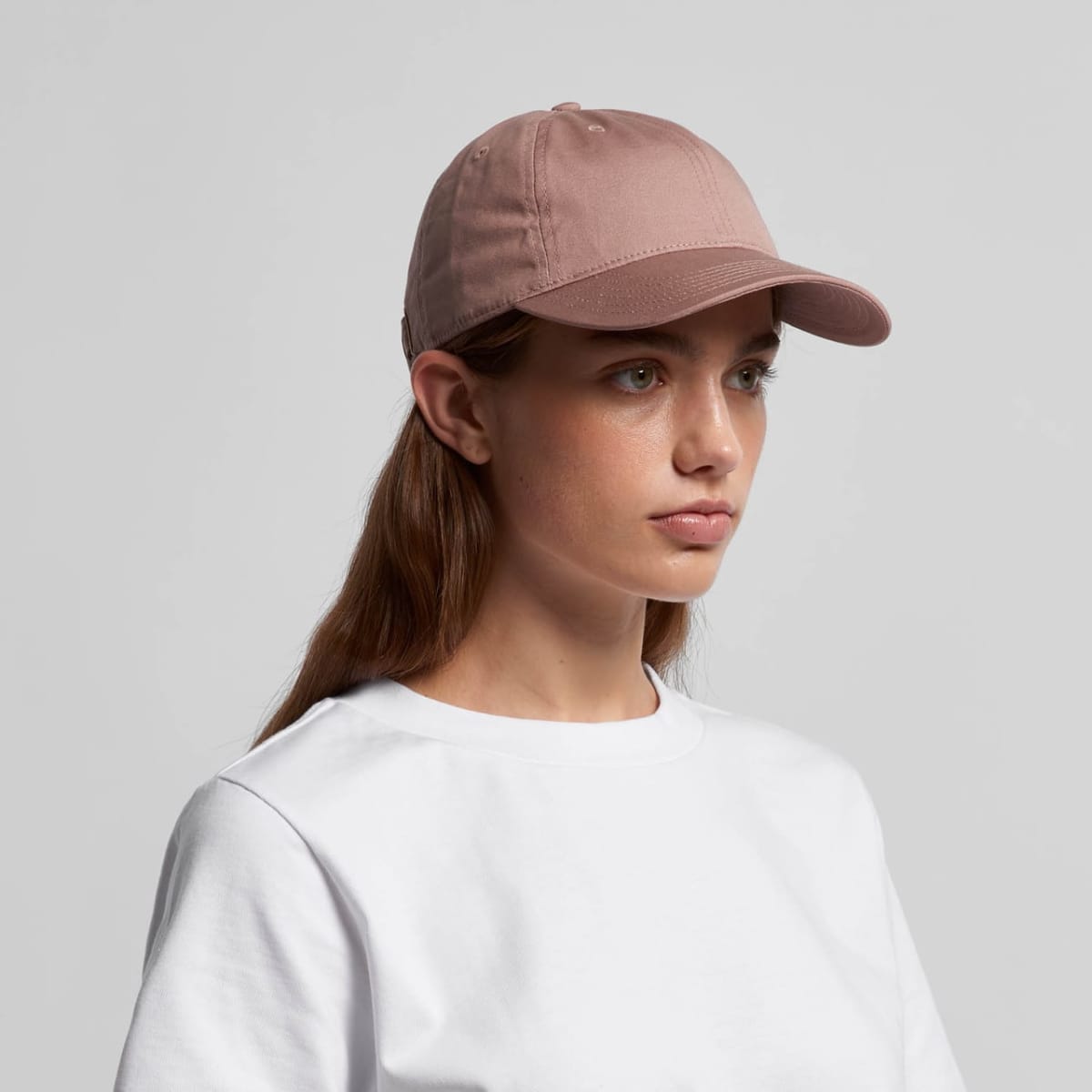 Woman wearing a light pink baseball cap and a plain white t-shirt, facing slightly right.