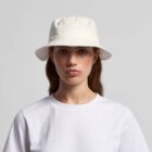 Woman in white bucket hat and white t-shirt, looking straight at the camera.