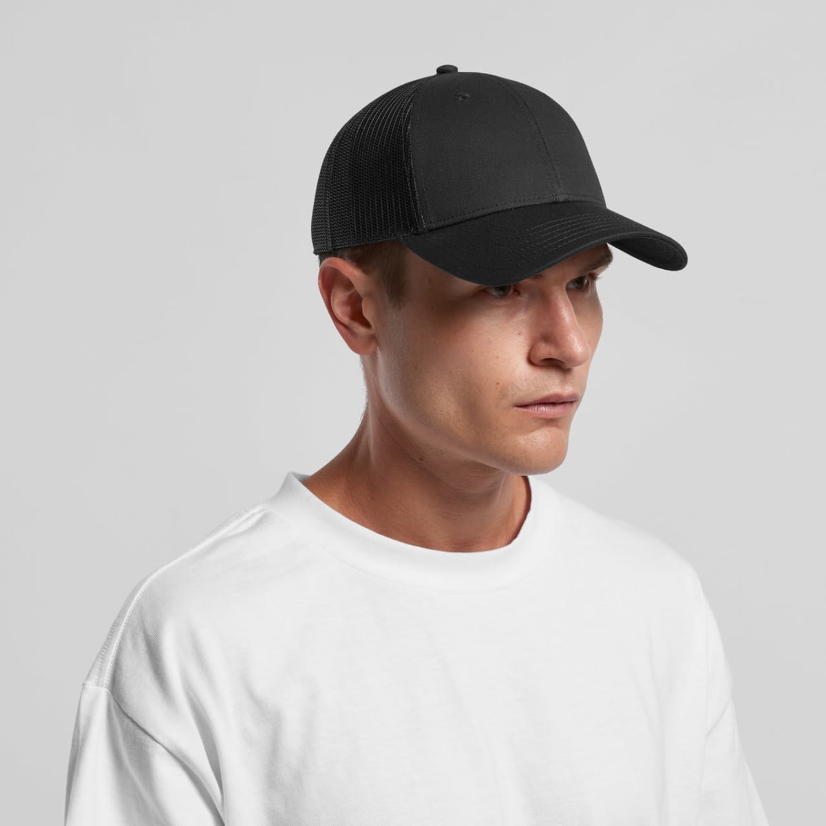 Person in a white t-shirt and black cap looking to the side against a plain background.