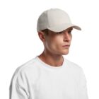 Man in a white t-shirt and beige baseball cap looking to the side on a white background.