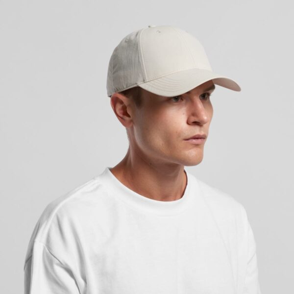 Man in a white t-shirt and light-colored cap looking to the side against a plain background.