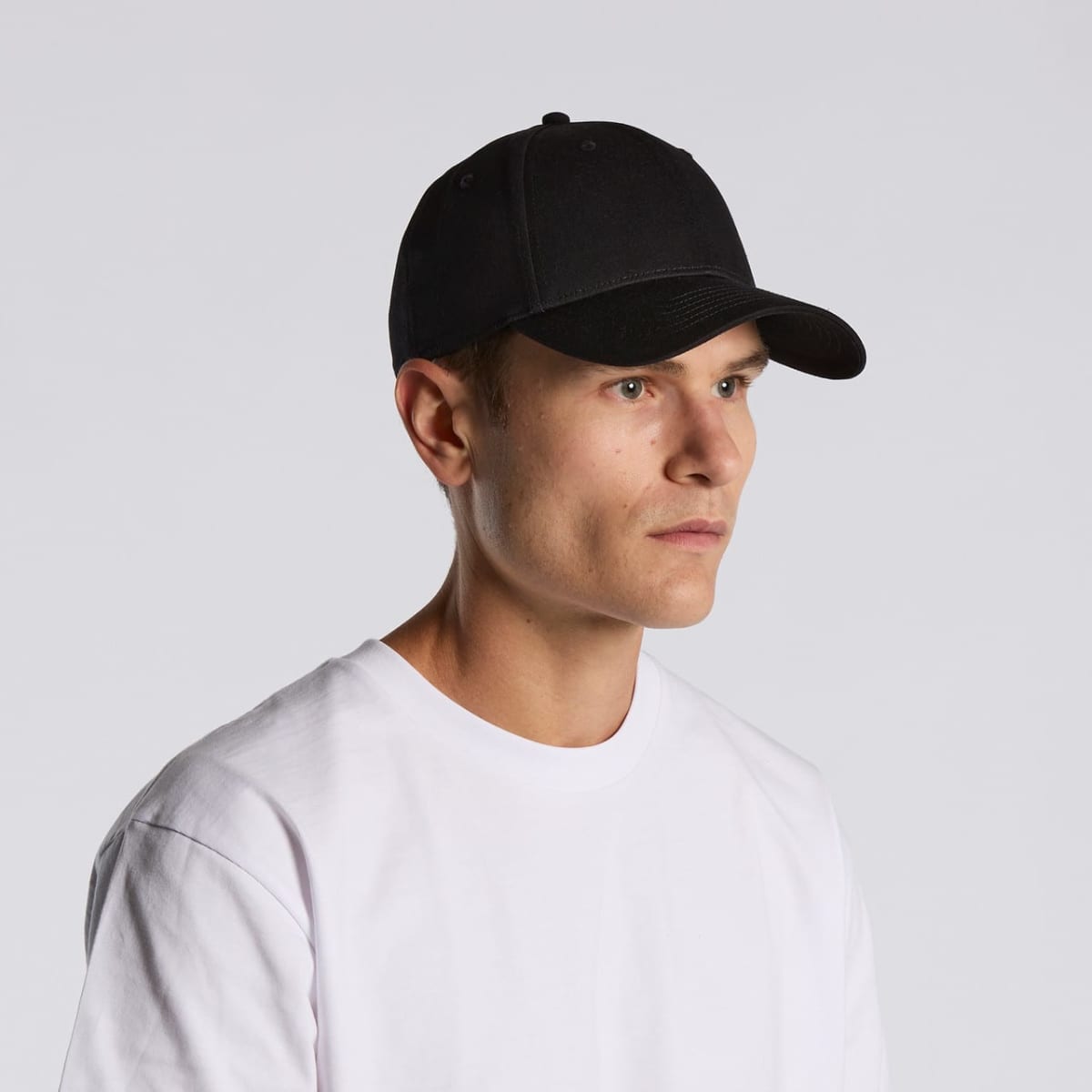 Man in a white t-shirt and black baseball cap looking to the side against a plain background.