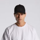 Man wearing a black cap and white t-shirt against a plain light background.