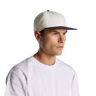Man in a white T-shirt and white cap with a dark brim, looking to the right.