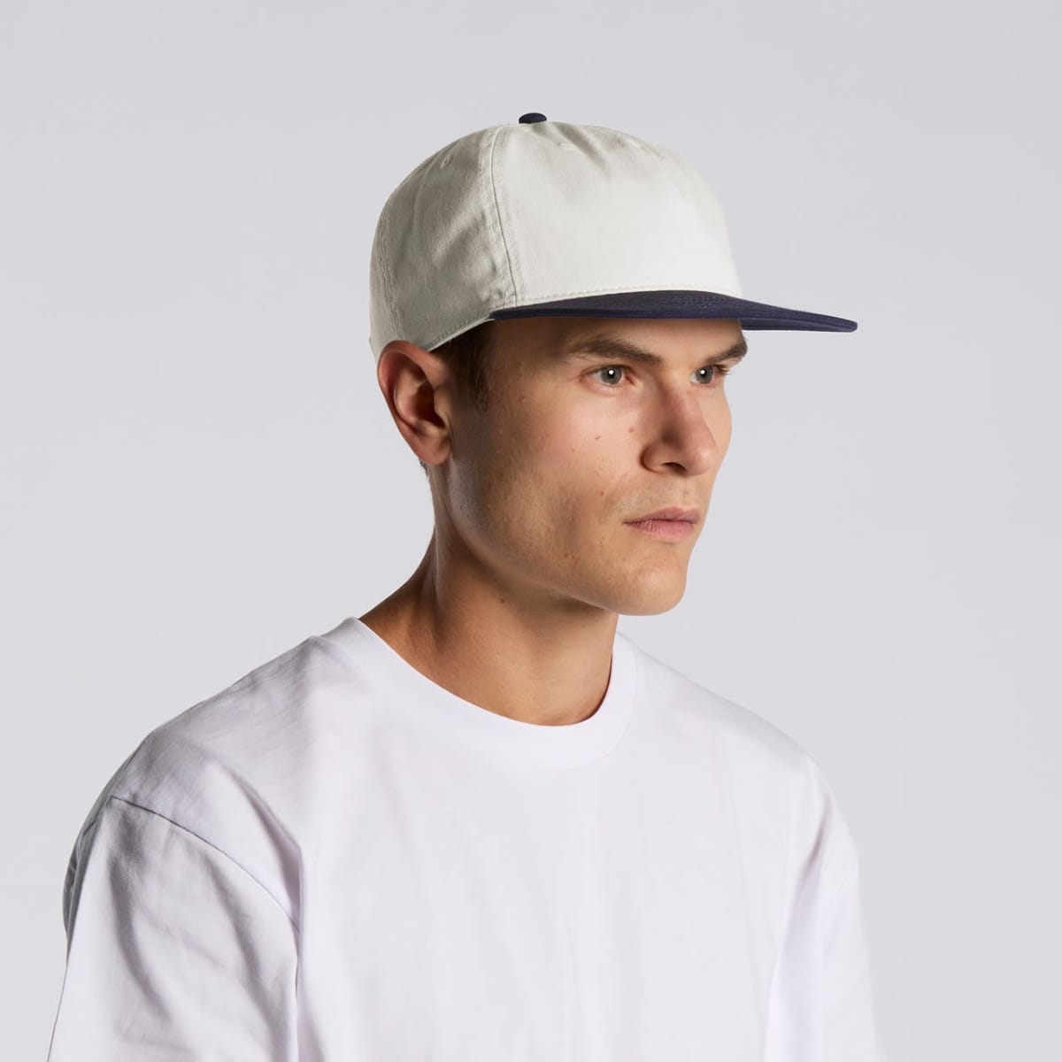 Man in a white t-shirt and white baseball cap with a dark brim, looking to the side.