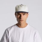 Serious man in white t-shirt and white cap looks straight at camera against plain background.