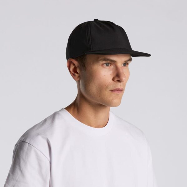 Man in white t-shirt and black cap looking to the side against a plain background.