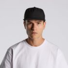 A man in a white t-shirt and black cap looks directly at the camera against a plain background.