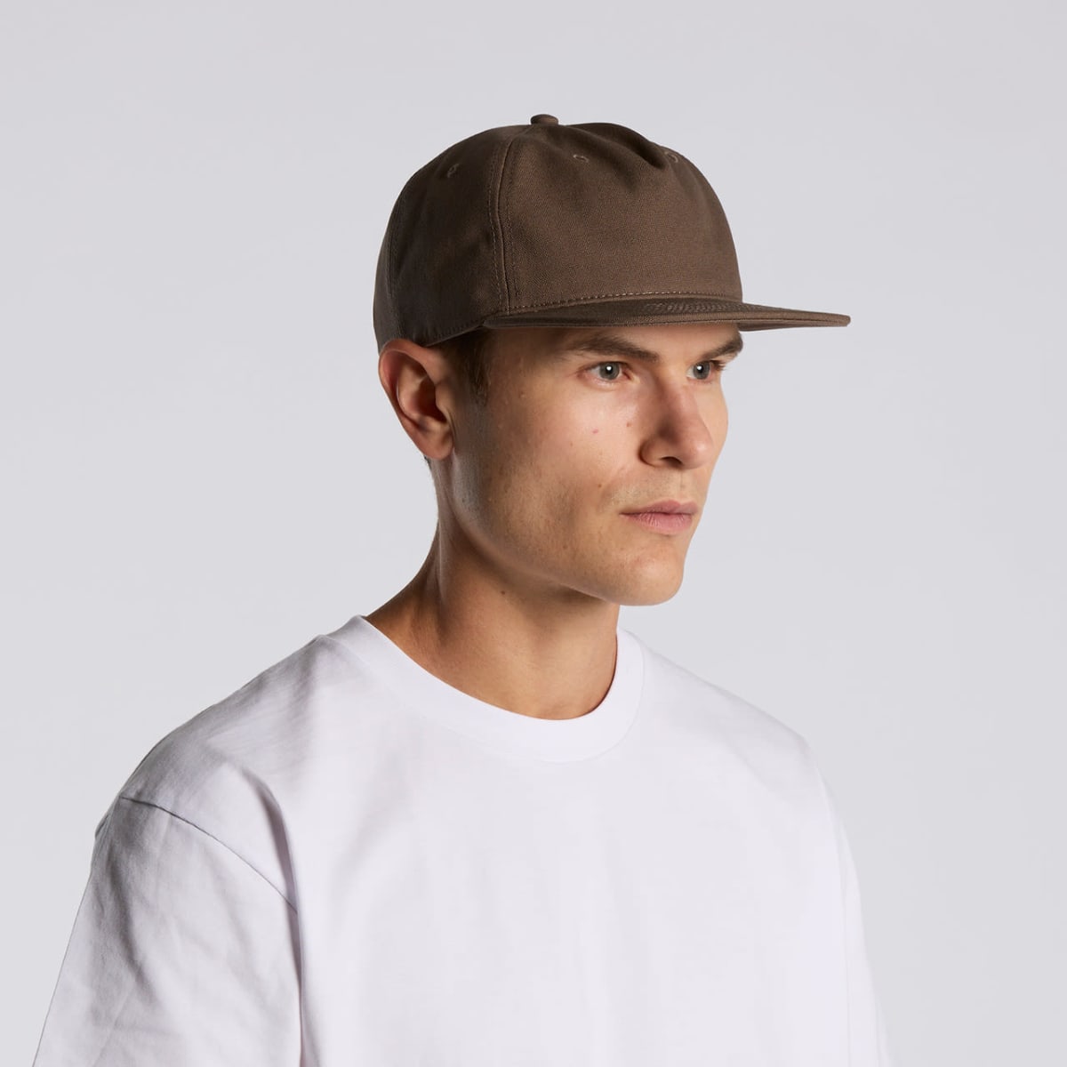 Man in a white t-shirt and brown baseball cap looking to the side against a plain background.