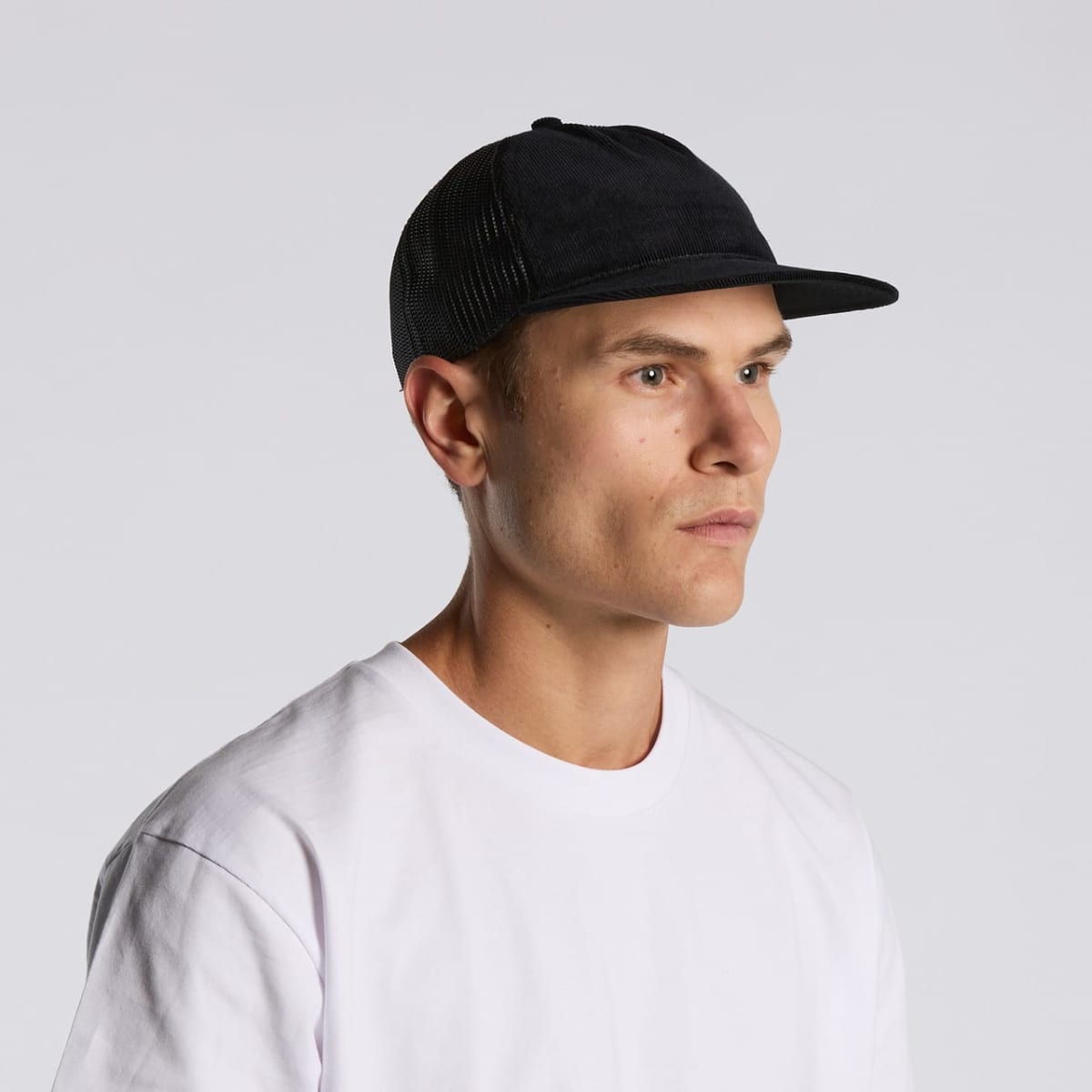 Man in a white t-shirt and black cap looking to the side against a plain background.