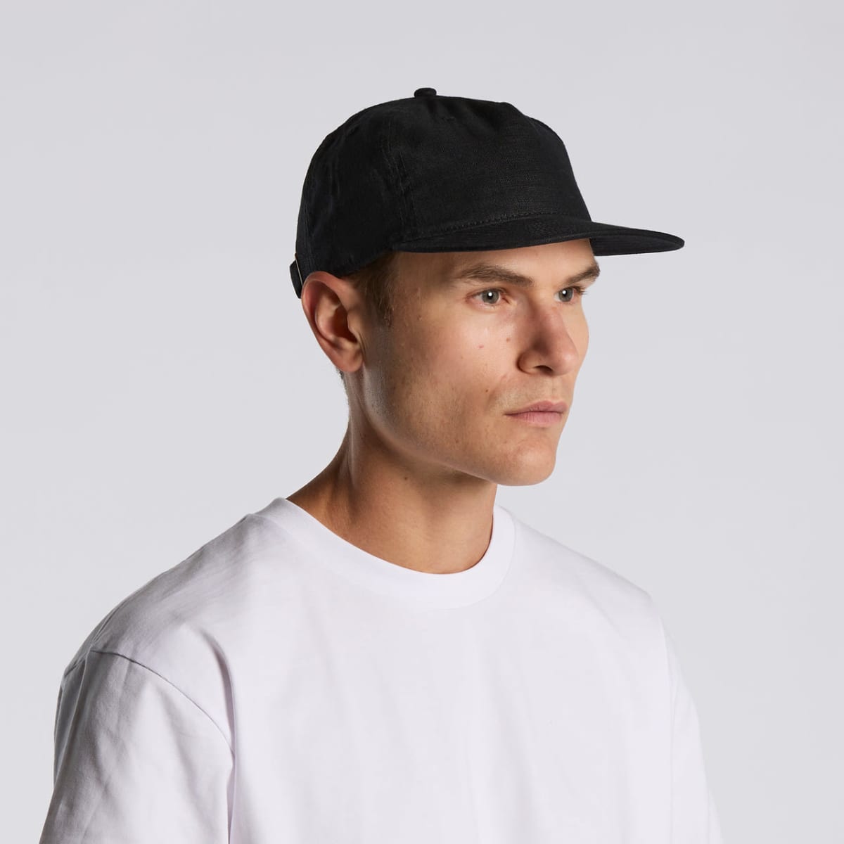 Man in a white t-shirt and black cap looking to the side against a plain background.