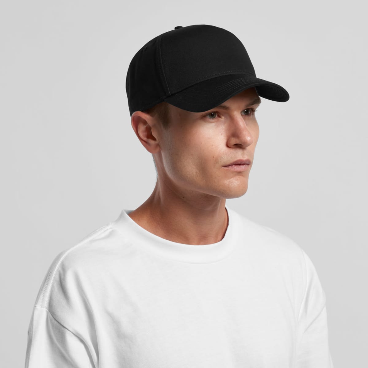 A person wearing a black baseball cap and a plain white shirt against a light background.