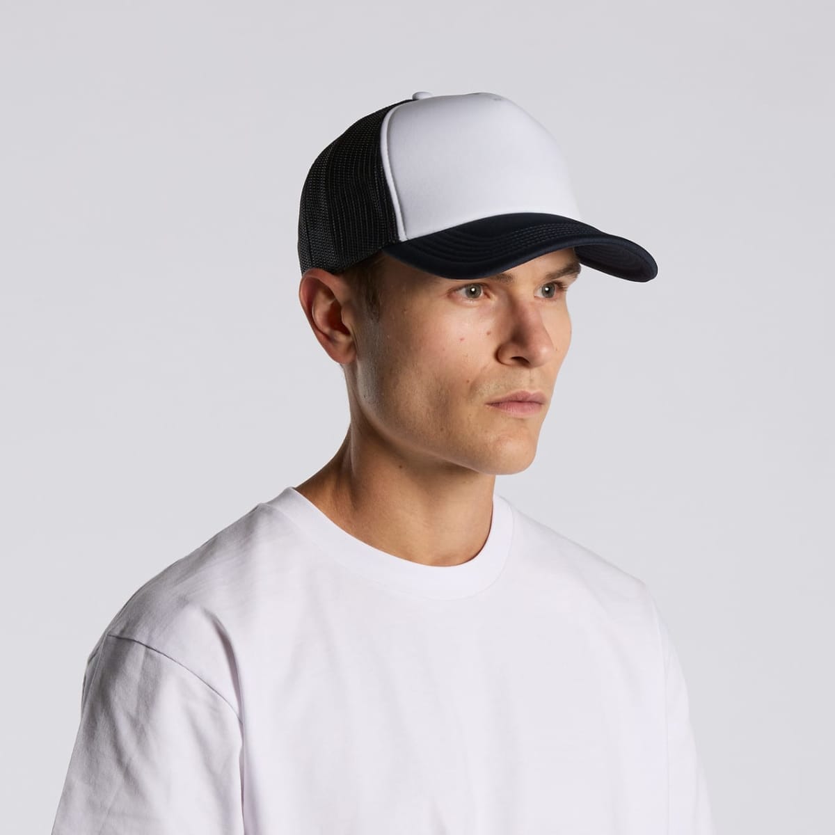 Man wearing a white t-shirt and a black-and-white trucker cap against a plain background.