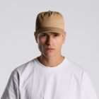 Person wearing a beige cap and white t-shirt against a plain light gray background.