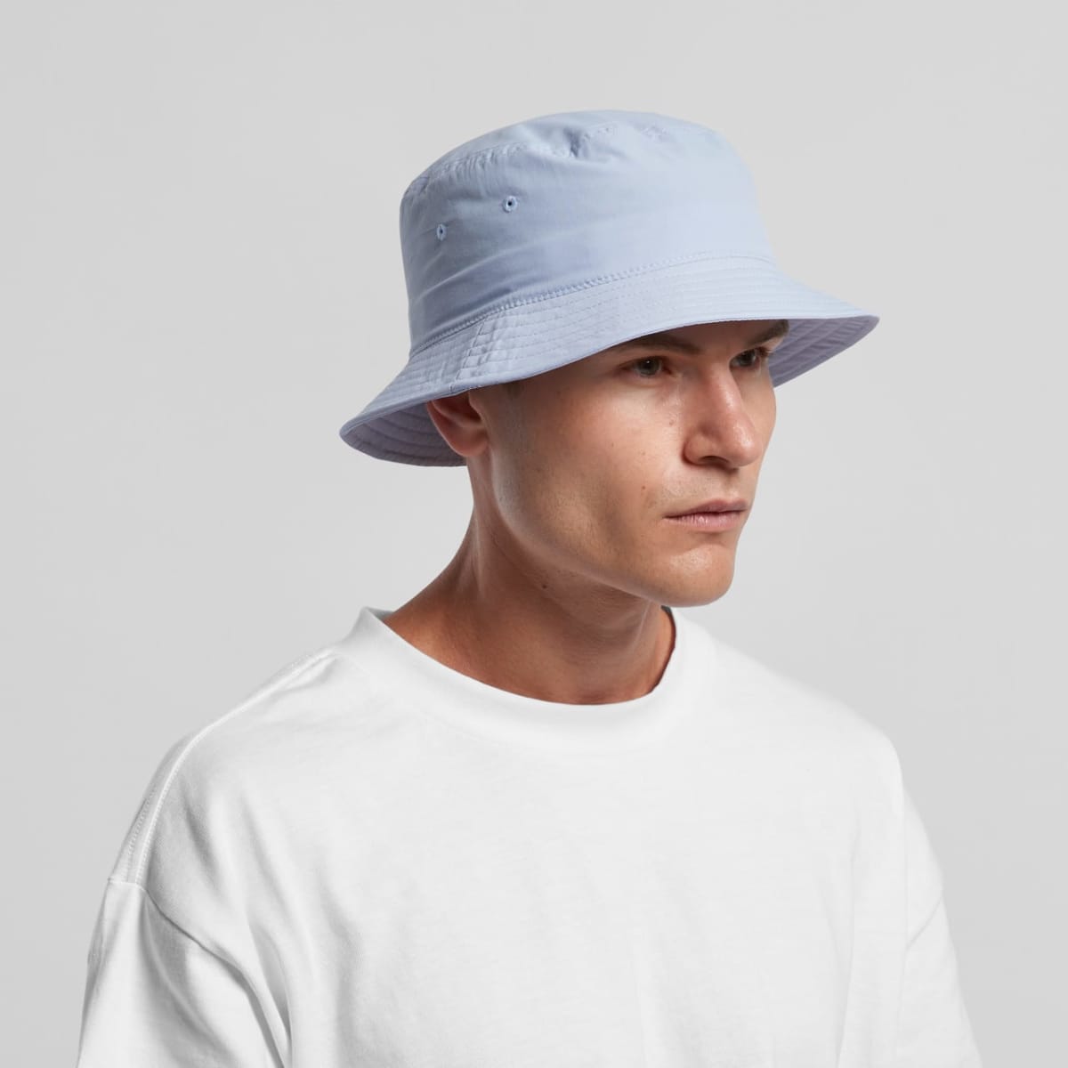 Man in a light blue bucket hat and white shirt looking to the side against a gray background.