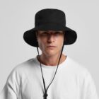 Young person in a white shirt wearing a black wide-brim bucket hat with chin straps.