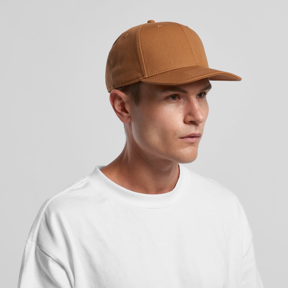 A person in a brown cap and white shirt looks to the side against a plain background.
