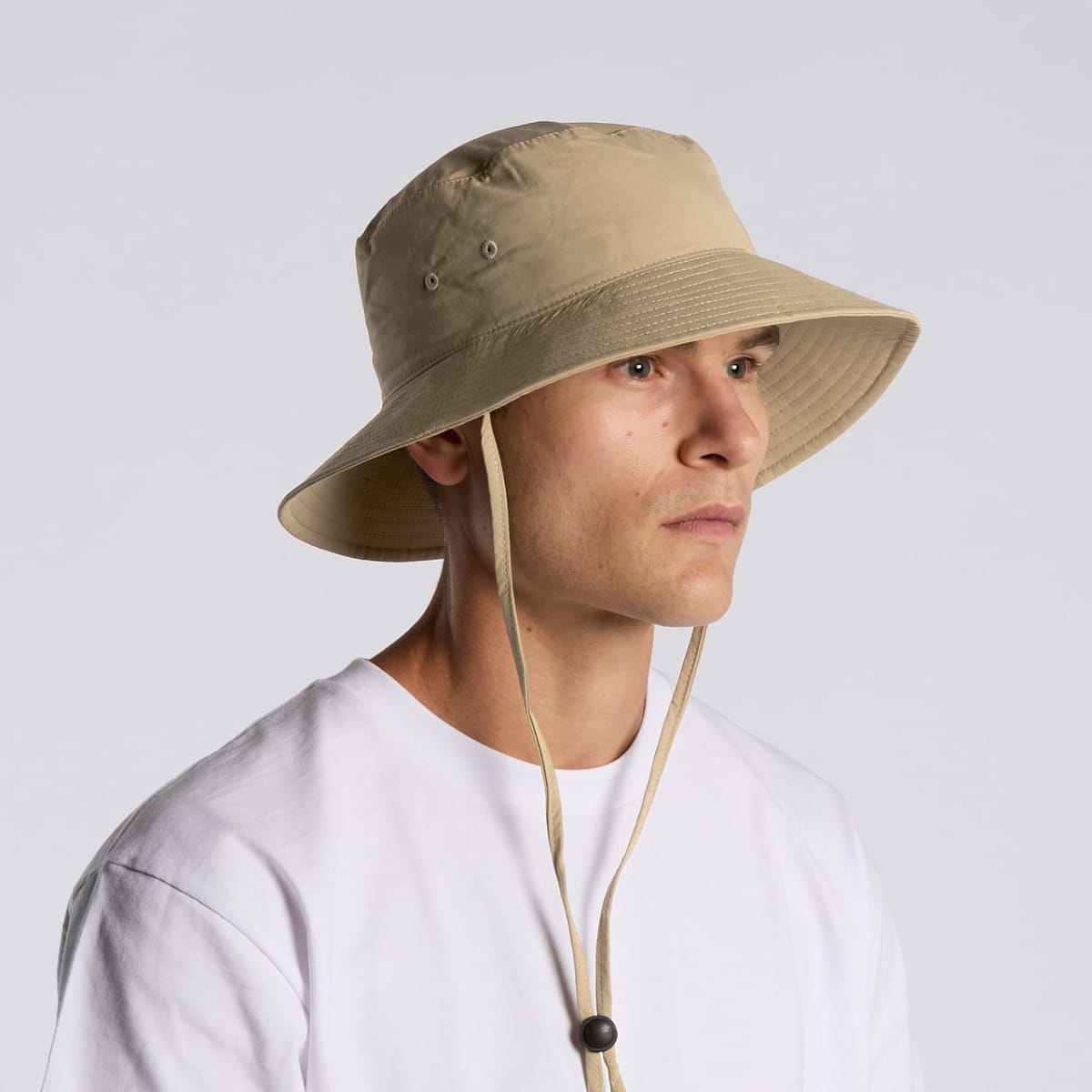 Man wearing a beige bucket hat with chin strap and a plain white shirt, facing right.