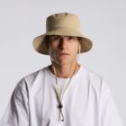 Person in a beige bucket hat and white shirt, facing forward against a plain background.