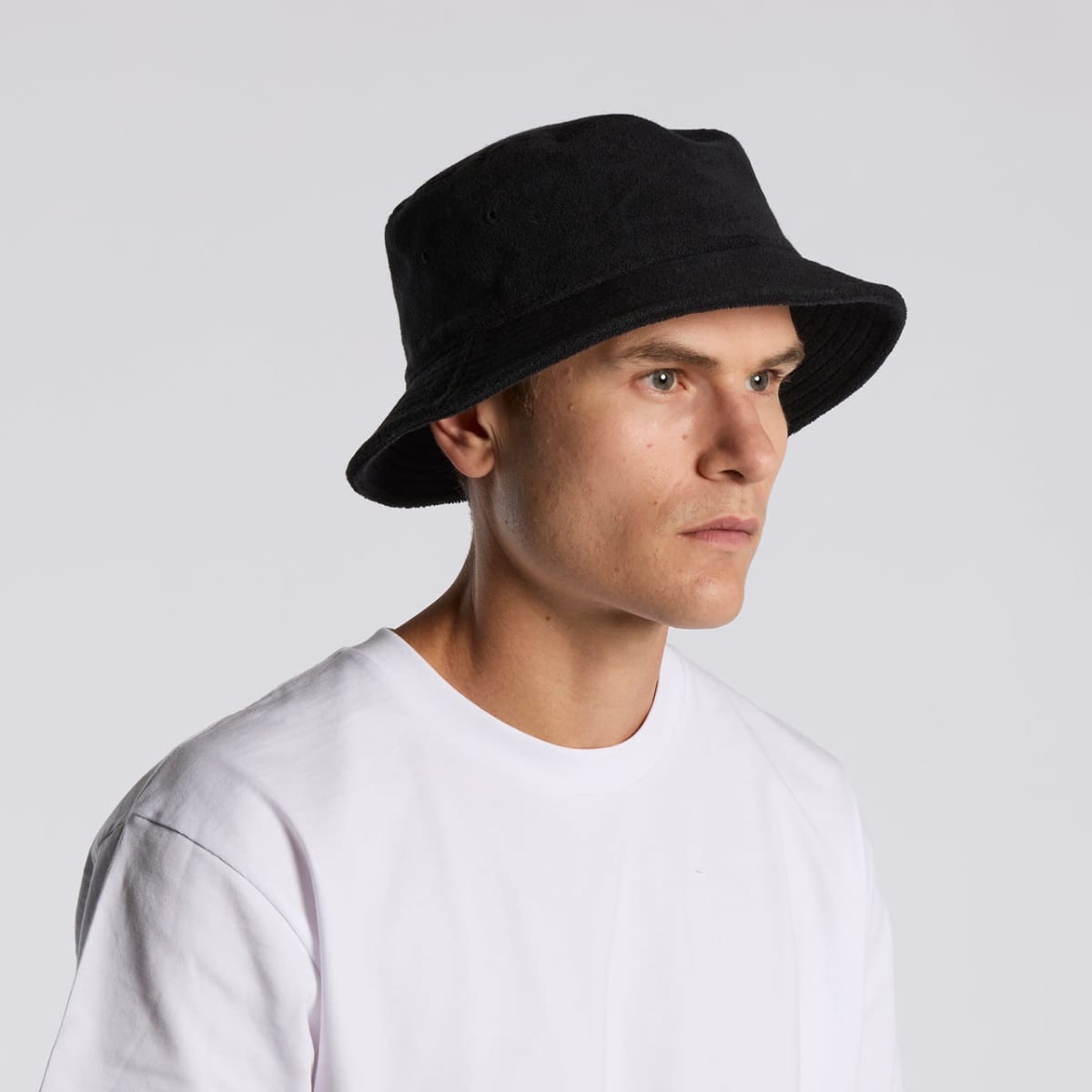 Man in a white shirt wearing a black bucket hat, looking to the side against a gray background.