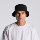 Man in a white shirt and black bucket hat looking at the camera against a plain background.
