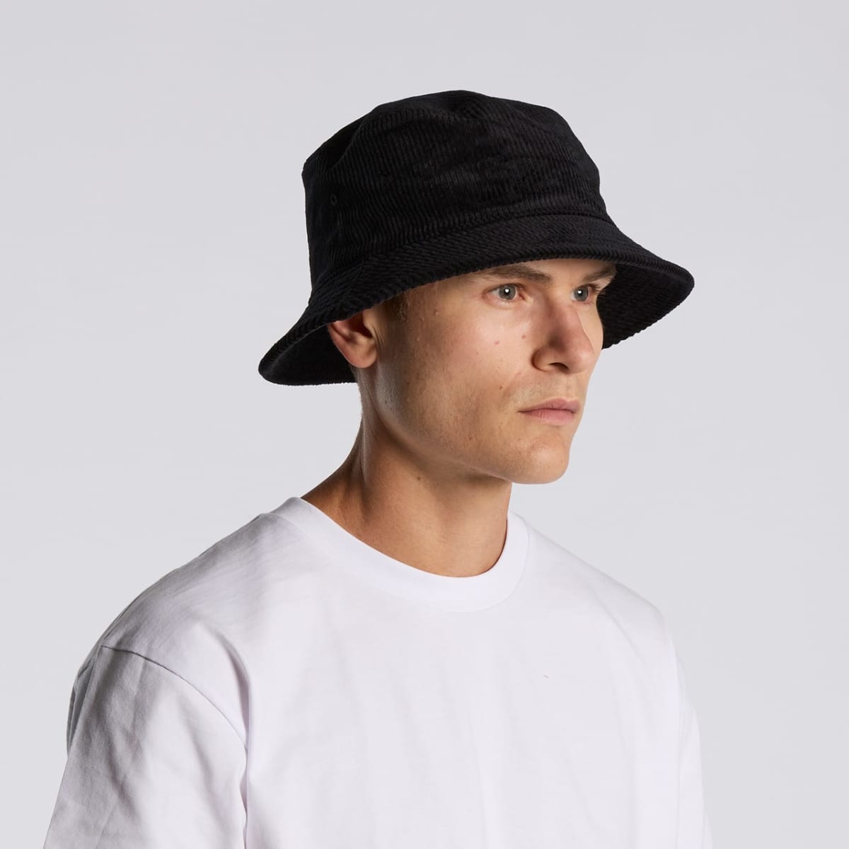 Man in a white shirt and black bucket hat looking to the side against a plain background.