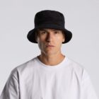 A person in a white shirt and black bucket hat looks at the camera with a neutral expression.