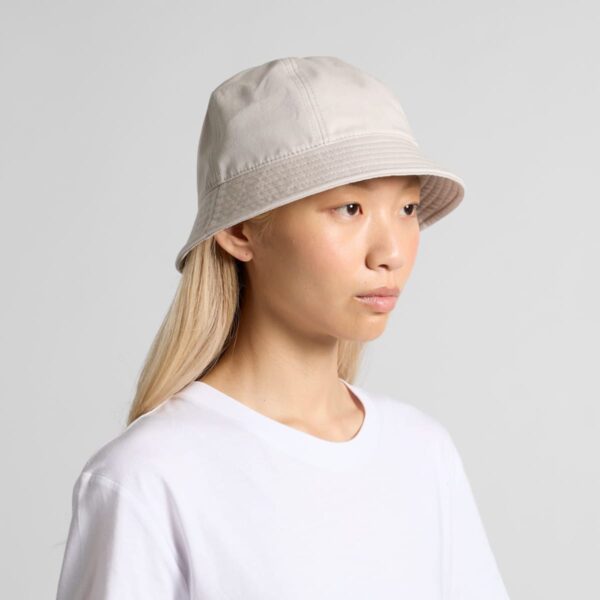 Person in a white t-shirt and beige bucket hat looking to the side against a light background.