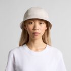 Person wearing a beige bucket hat and white t-shirt against a plain background.