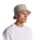 A person wearing a beige bucket hat and a white t-shirt against a white background.